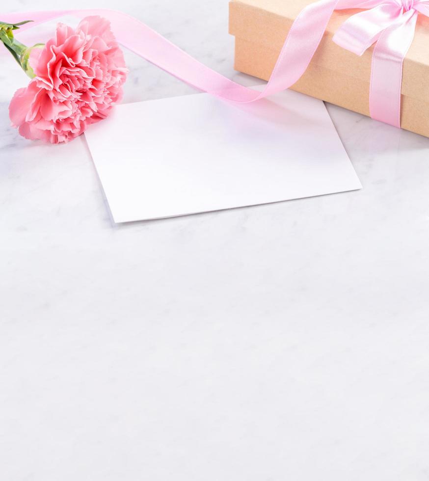 May mothers day handmade giftbox idea concept, beautiful blooming carnations with baby pink ribbon bow gift isolated on modern marble desk, close up, copy space, mock up photo