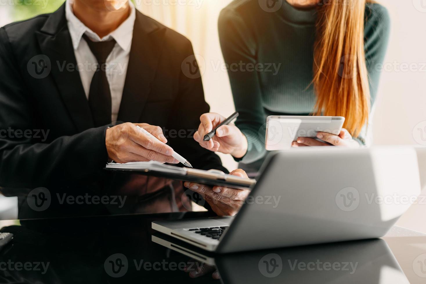 Business documents on office table with smart phone and laptop and two colleagues discussing data in the background photo