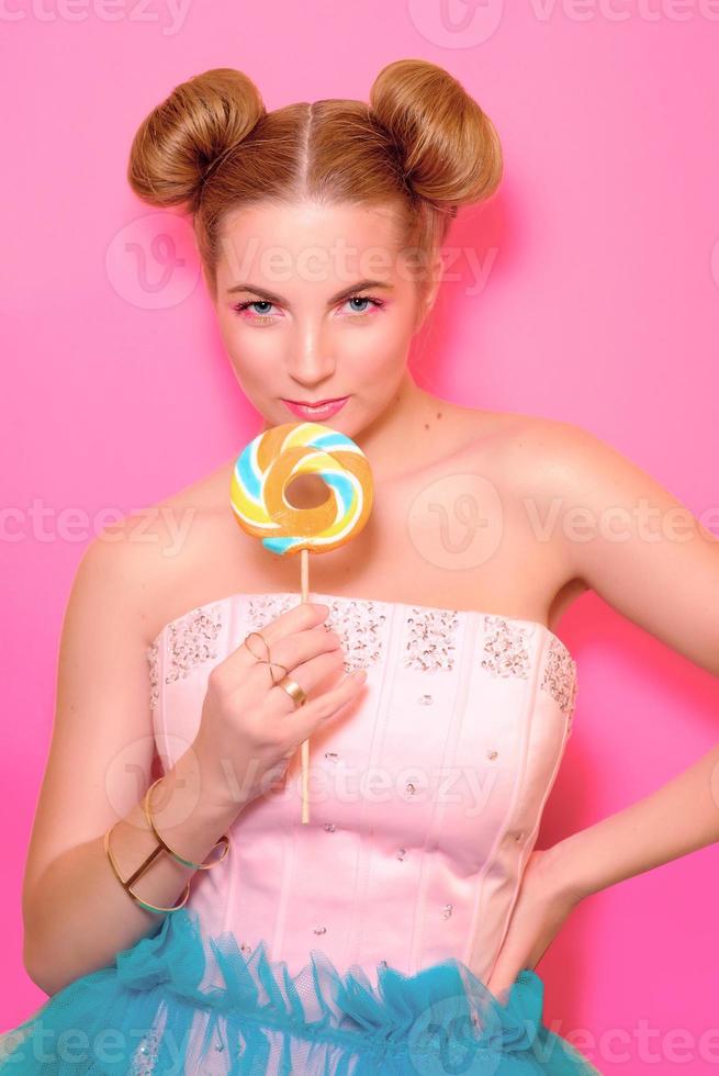 Portrait of stylish cute young blonde woman with colorful lollipop on pink background photo