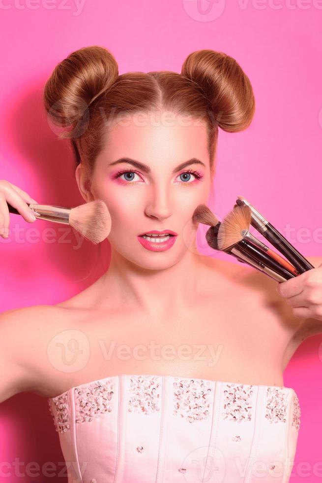 atractiva mujer rubia con maquillaje colorido con pinceles cosméticos y sombras en ella y maquilla las manos del maestro foto