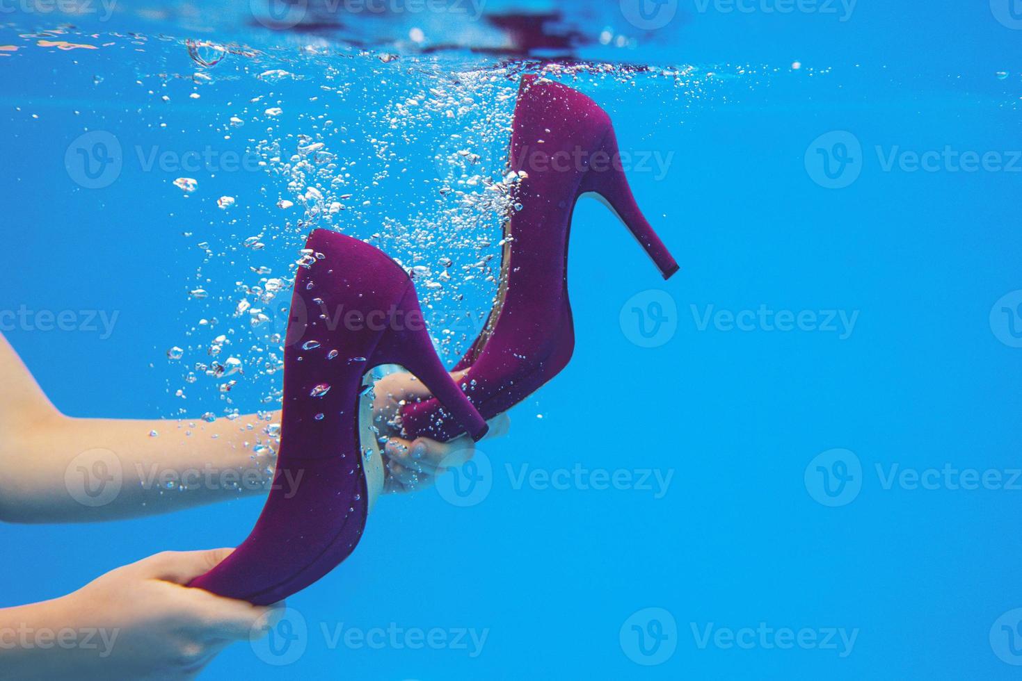 Violet velvet shoes in woman hands underwater in the swimming pool on blue background photo