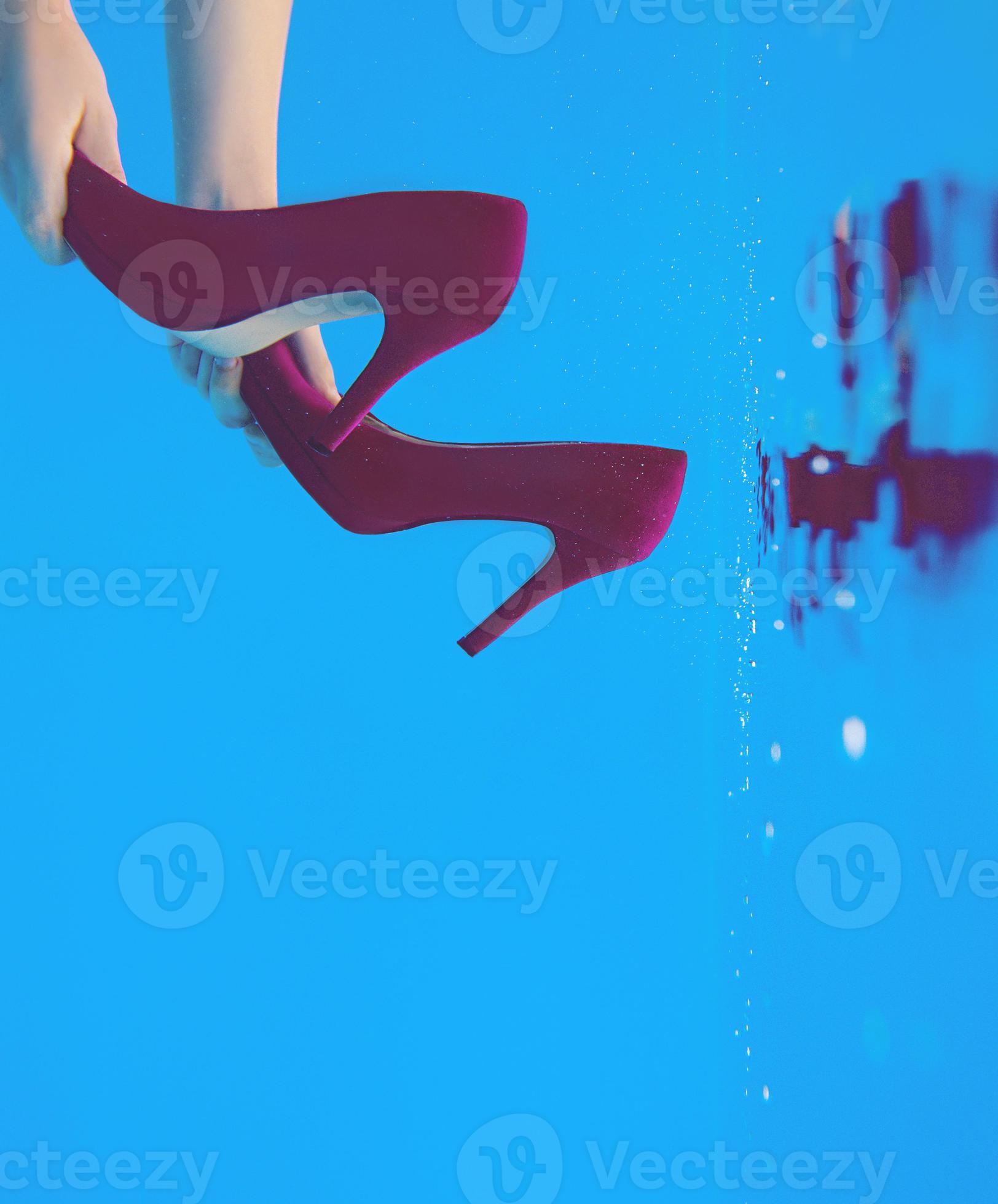 Violet velvet shoes in woman hands underwater in the swimming pool on