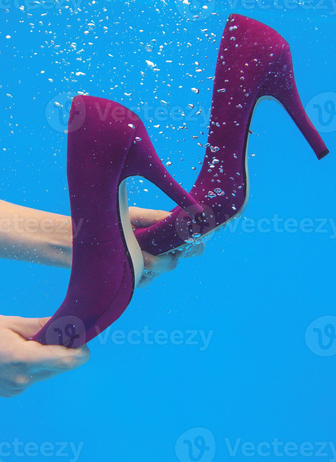 Violet velvet shoes in woman hands underwater in the swimming pool on