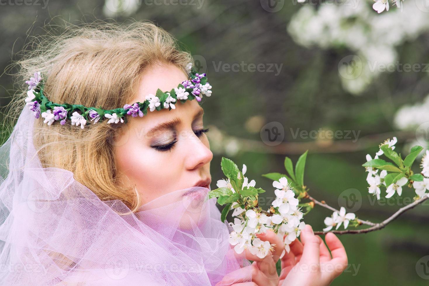 beautiful young blonde woman in flower wreath blooming trees in spring photo