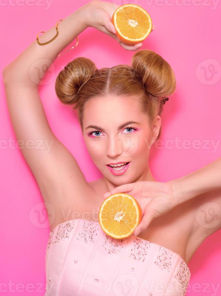 Portrait of stylish cute young blonde woman with oranges on pink background photo