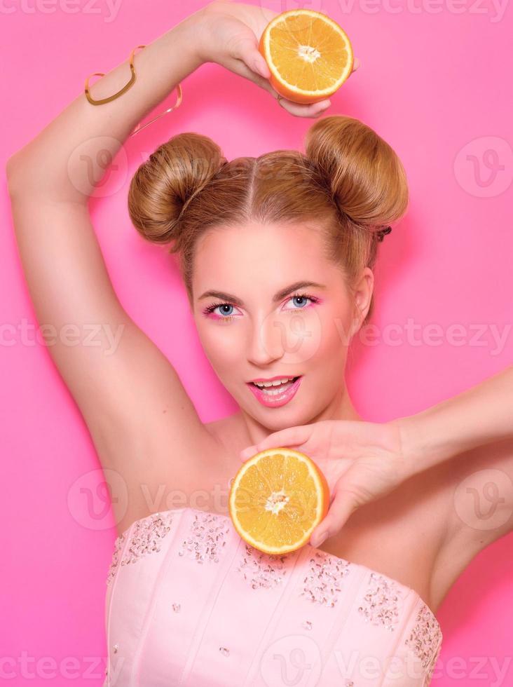 Portrait of stylish cute young blonde woman with oranges on pink background photo