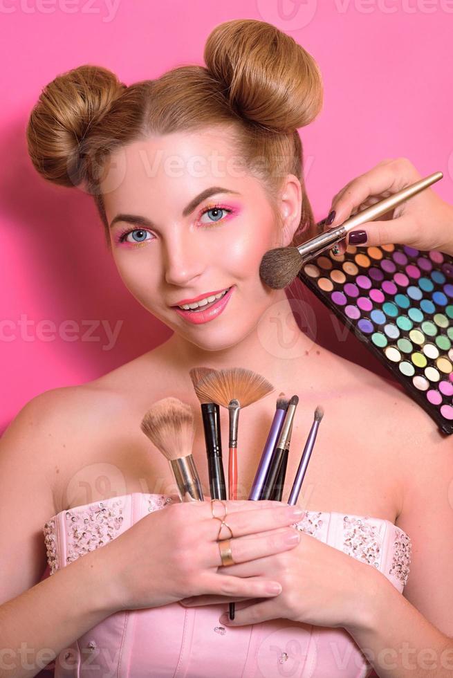 attractive blonde woman with colorful make up with cosmetic brushes and shadows in her and make up master's hands photo