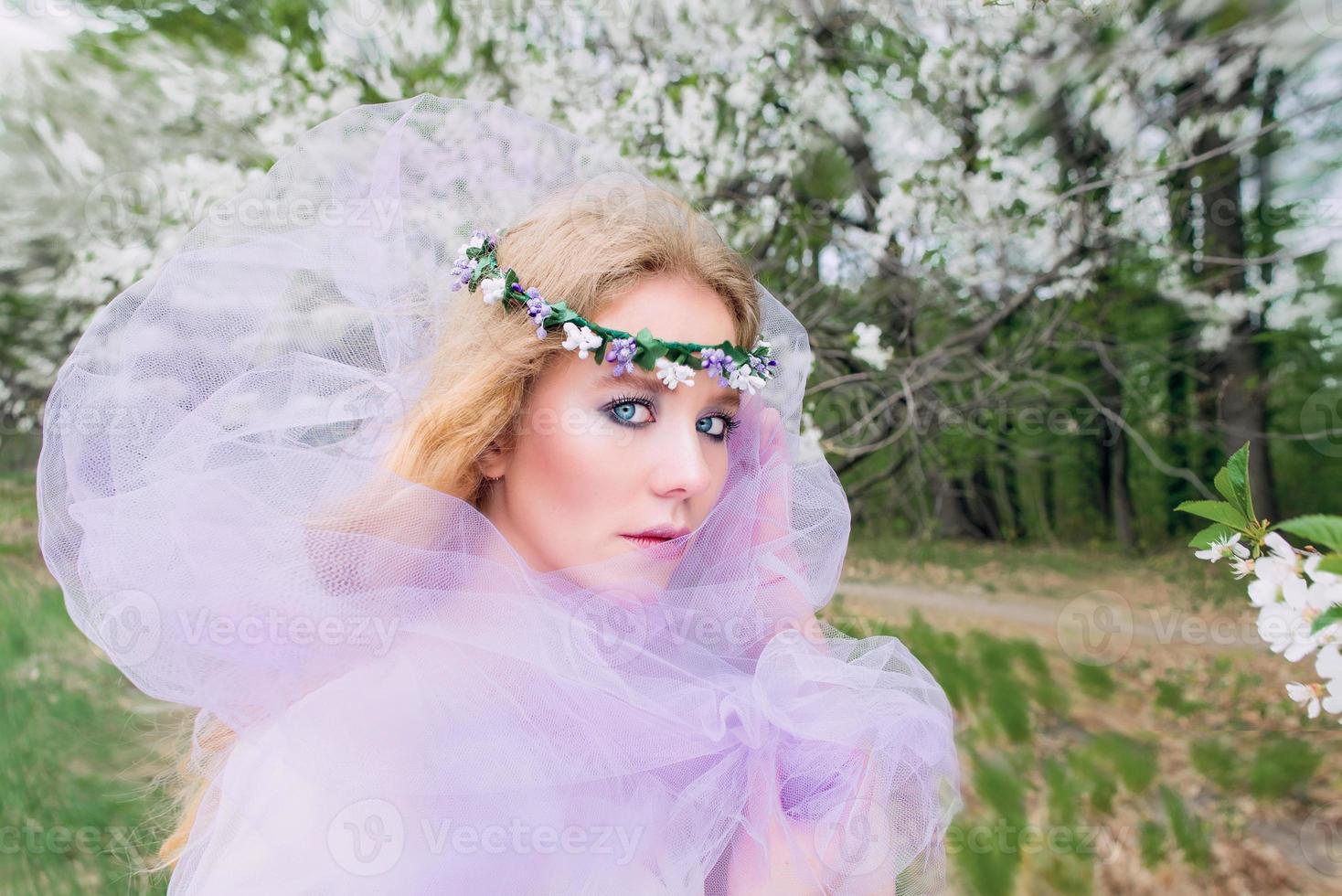 beautiful young blonde woman in flower wreath blooming trees in spring photo