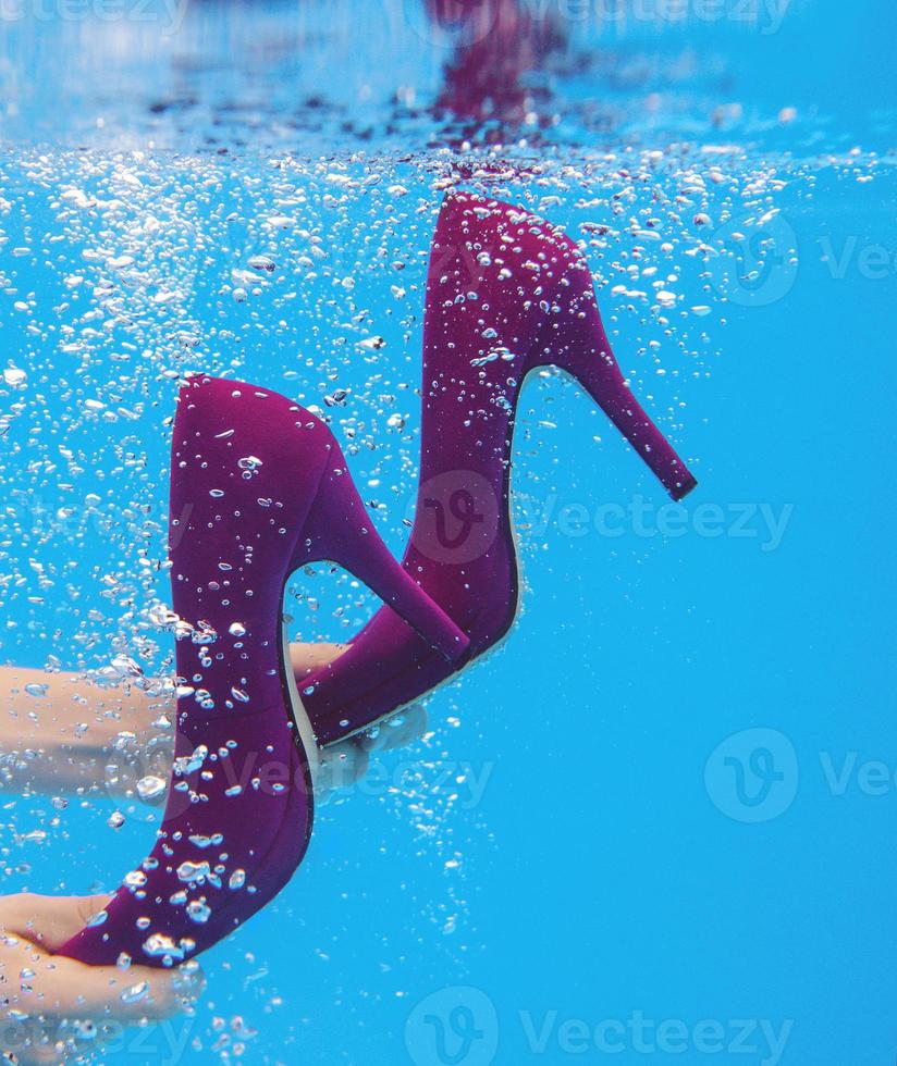 Violet velvet shoes in woman hands underwater in the swimming pool on