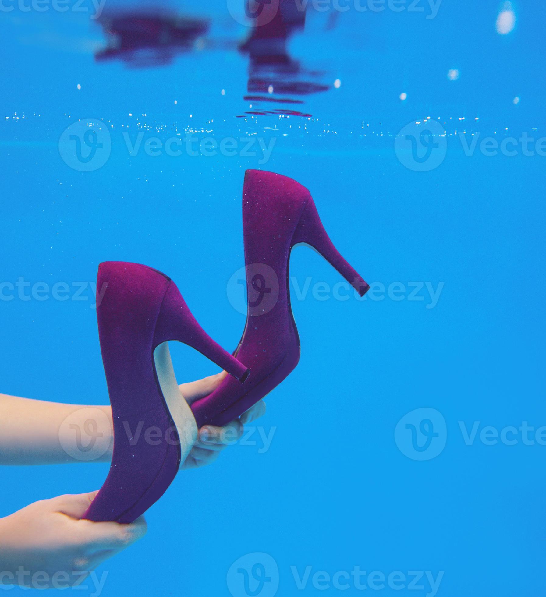 Violet velvet shoes in woman hands underwater in the swimming pool on