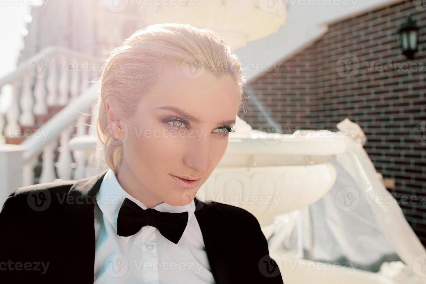 Portrait of stylish fashionable beautiful blonde woman in man black suit with bow tie outdoor photo