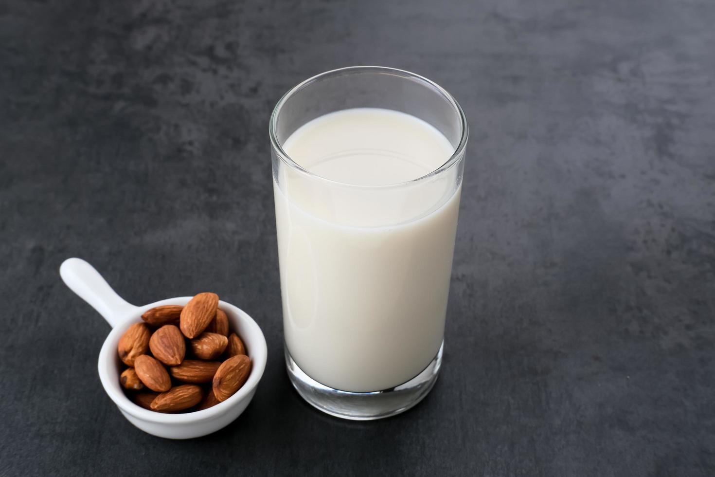 Almond milk in glass with almonds on wooden table. Space for text photo