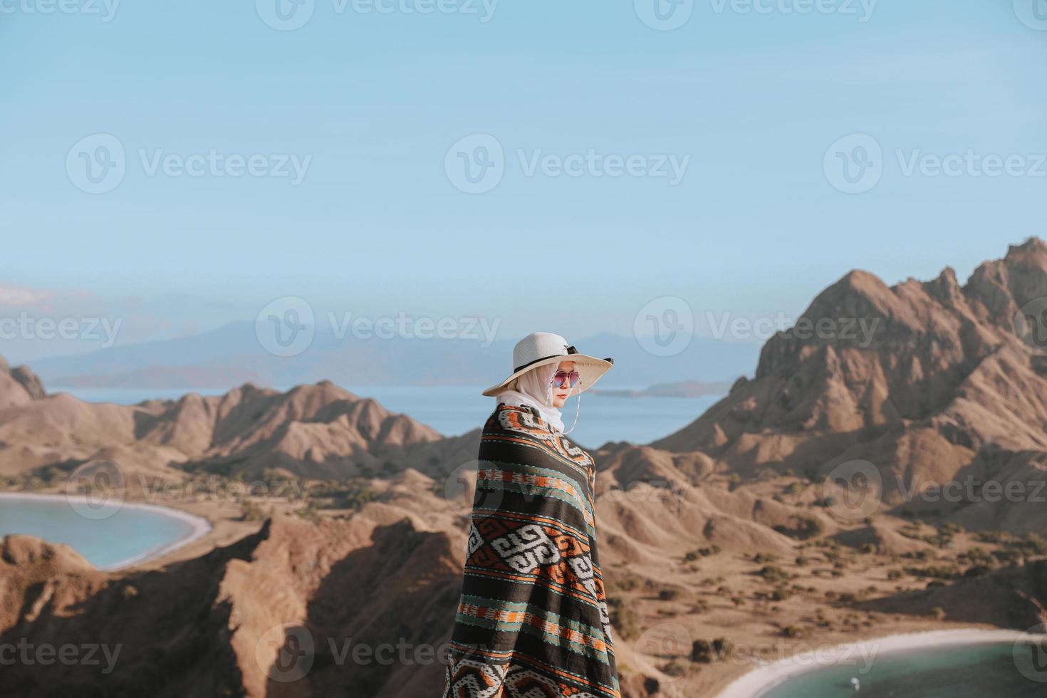 Stylish asian woman in summer hat and Indonesian traditional fabric called kain songket posing with background of hills and copy space on the sky photo