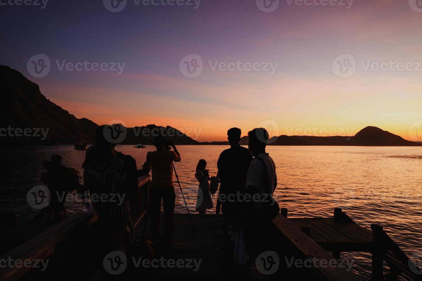 silueta negra de turistas reuniéndose y haciendo sesiones de fotos con mar y colinas en labuan bajo