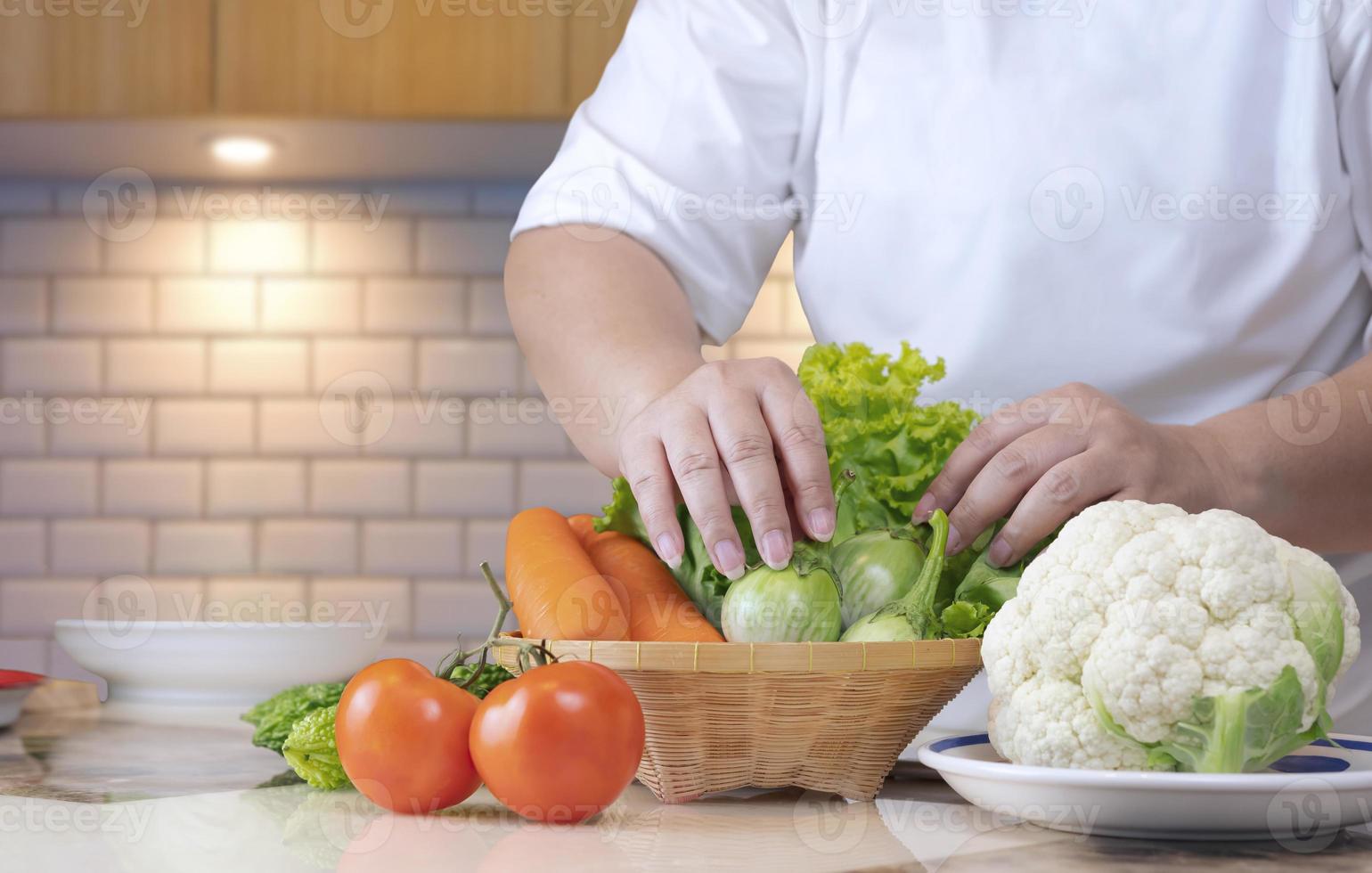 Close up of overweight woman hand preparing various organic vegetables into bamboo basket for cooking on kitchen table, healthy lifestyle concept photo