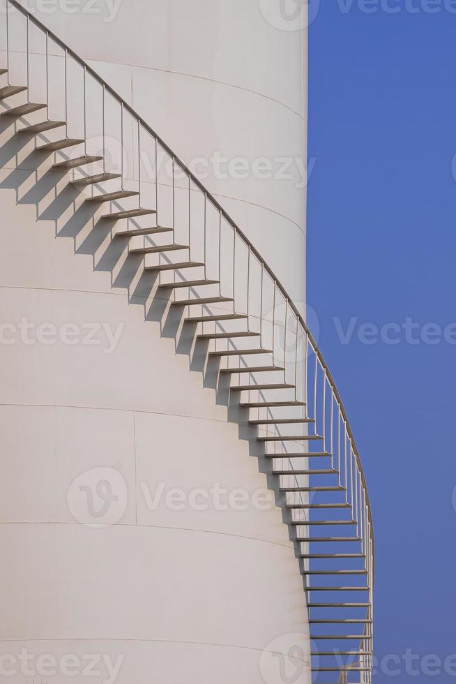Curved line of spiral staircase on oil storage fuel tank with blue sky in vertical frame photo