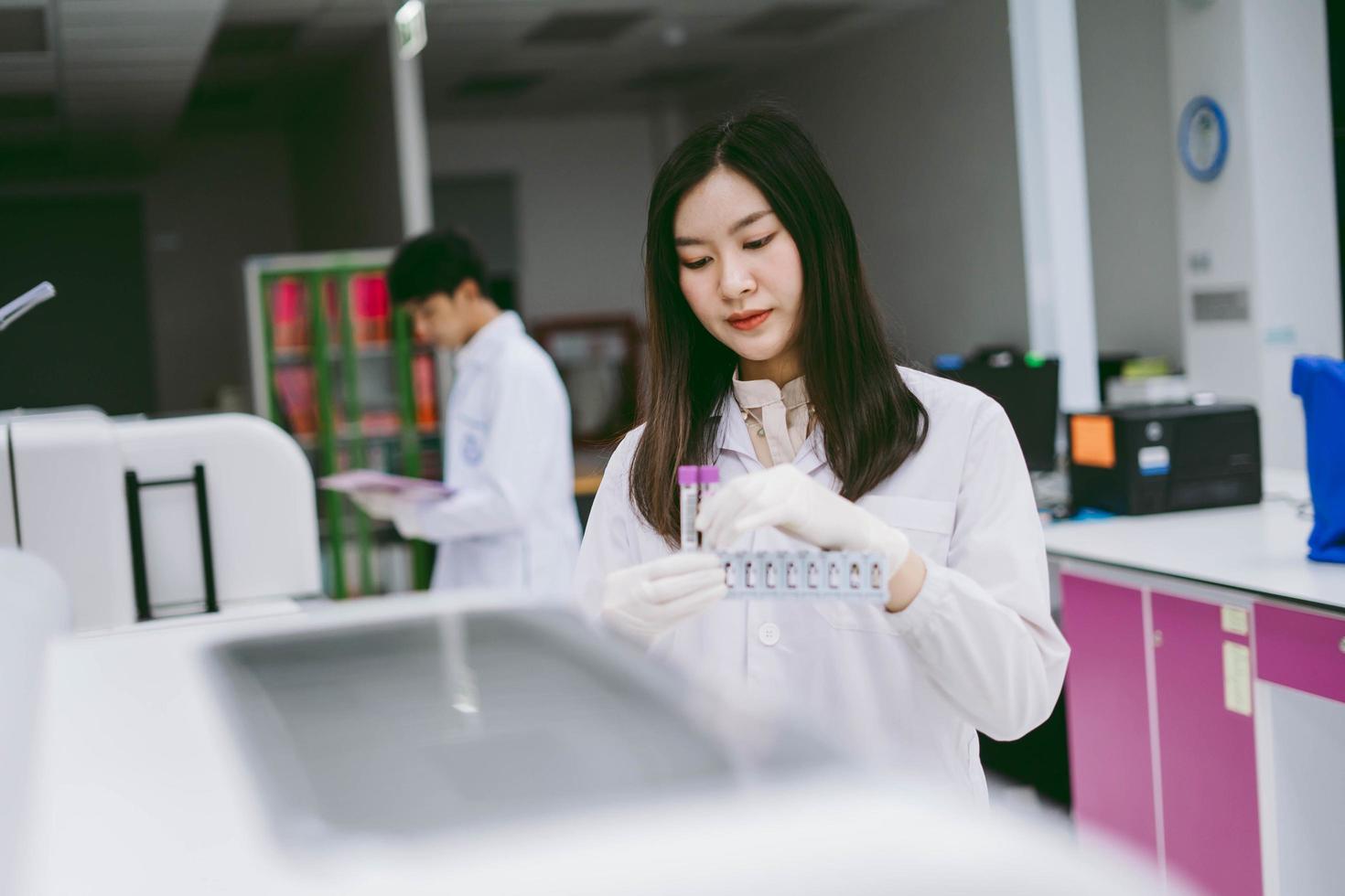 joven científica que trabaja con el informe del analizador de sangre de automatización en el laboratorio médico foto