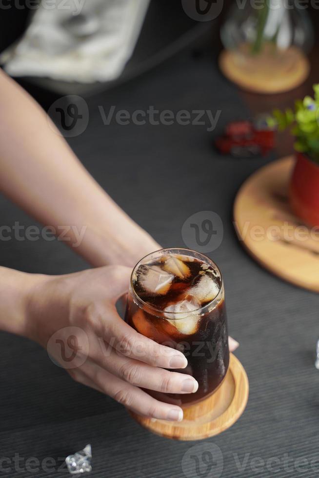 Hands holding a glass of espresso with lemon juice and fresh sliced lemon on wooden table and copy space, Summer Cocktail, Cold brew coffee or black tea. photo