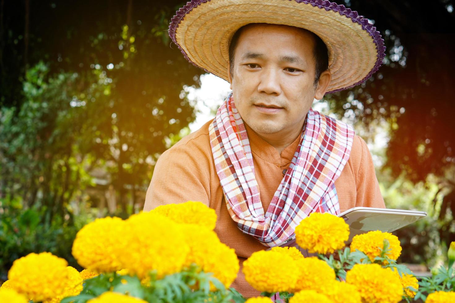 Asian middle aged man is relaxing with his free time by using his taplet to take photos and to store the growing data beside the vegetable beds in the backyard of his house. Soft and selective focus.