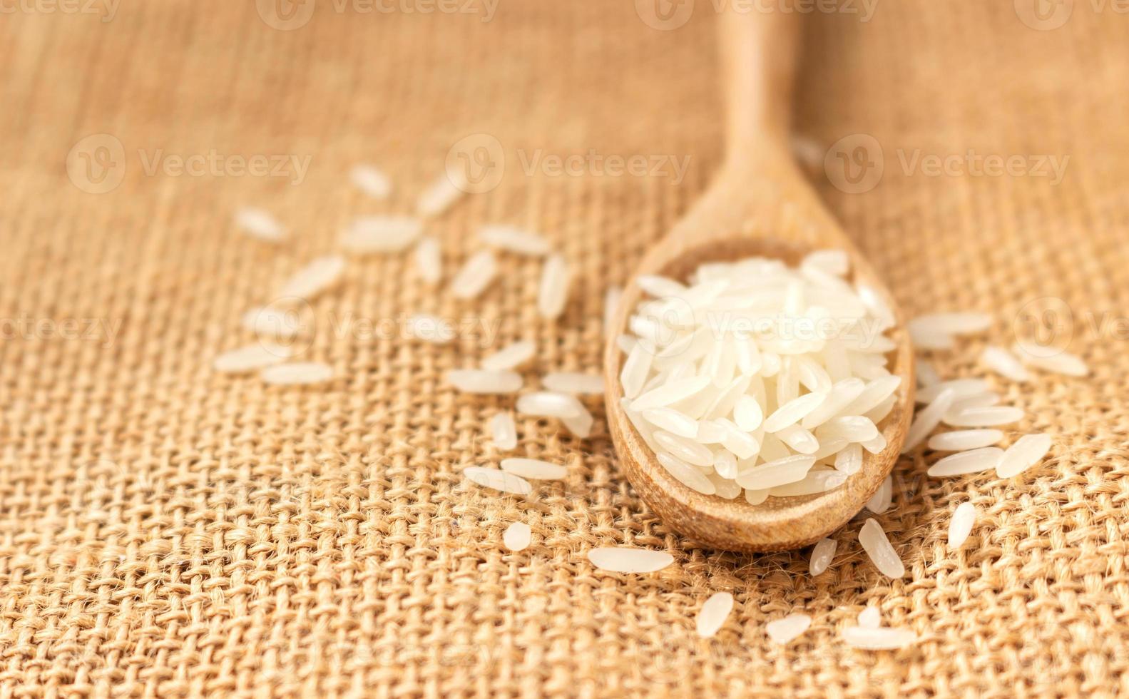 cerrar el grano de arroz crudo en una cuchara de madera sobre tela de saco foto