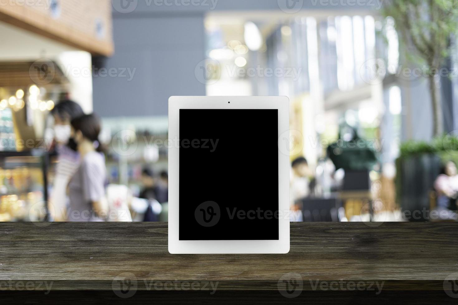 tablet with blank screen on black wooden table with blurred background in the coffee cafe, warm light tone. photo