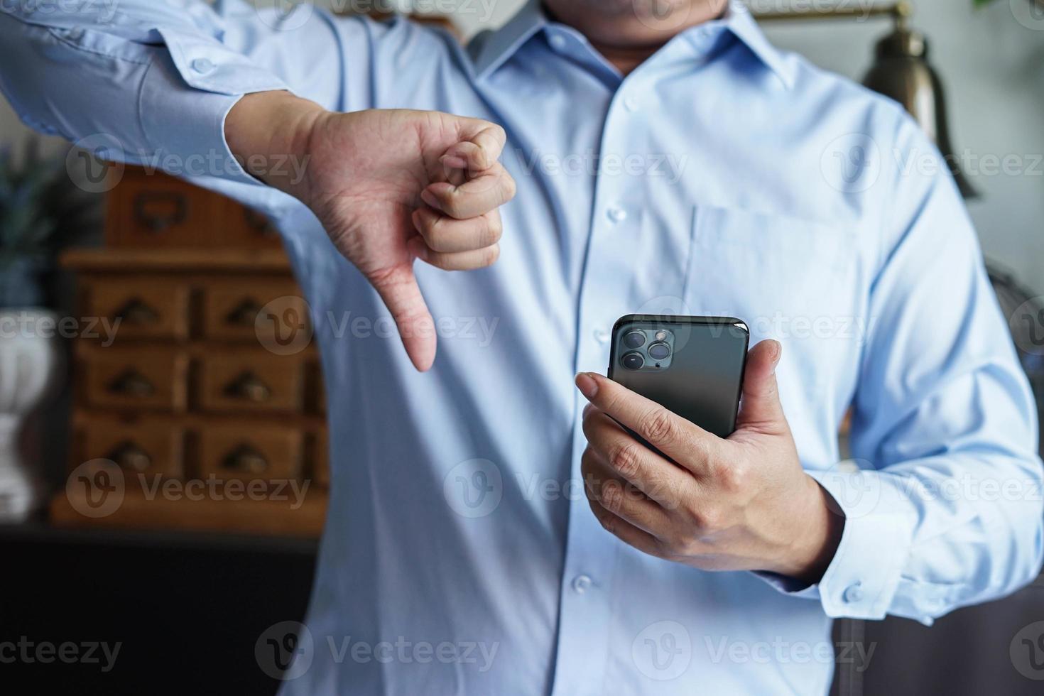 businessman give a thumb down with mobile phone for review product and comment. photo