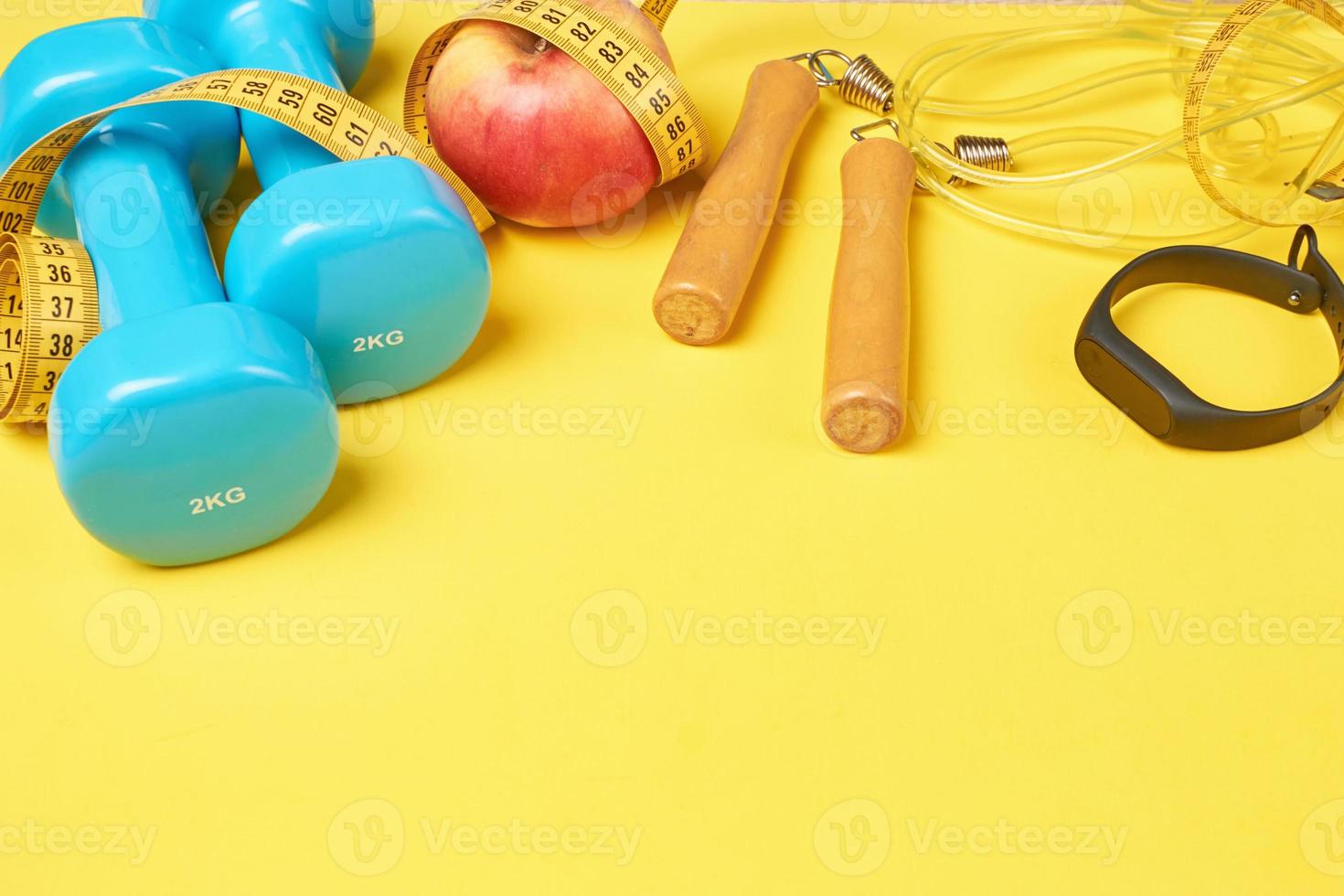 Fitness concept with blue dumbbells, jump rope and fitness tracker on a yellow background, copy space photo