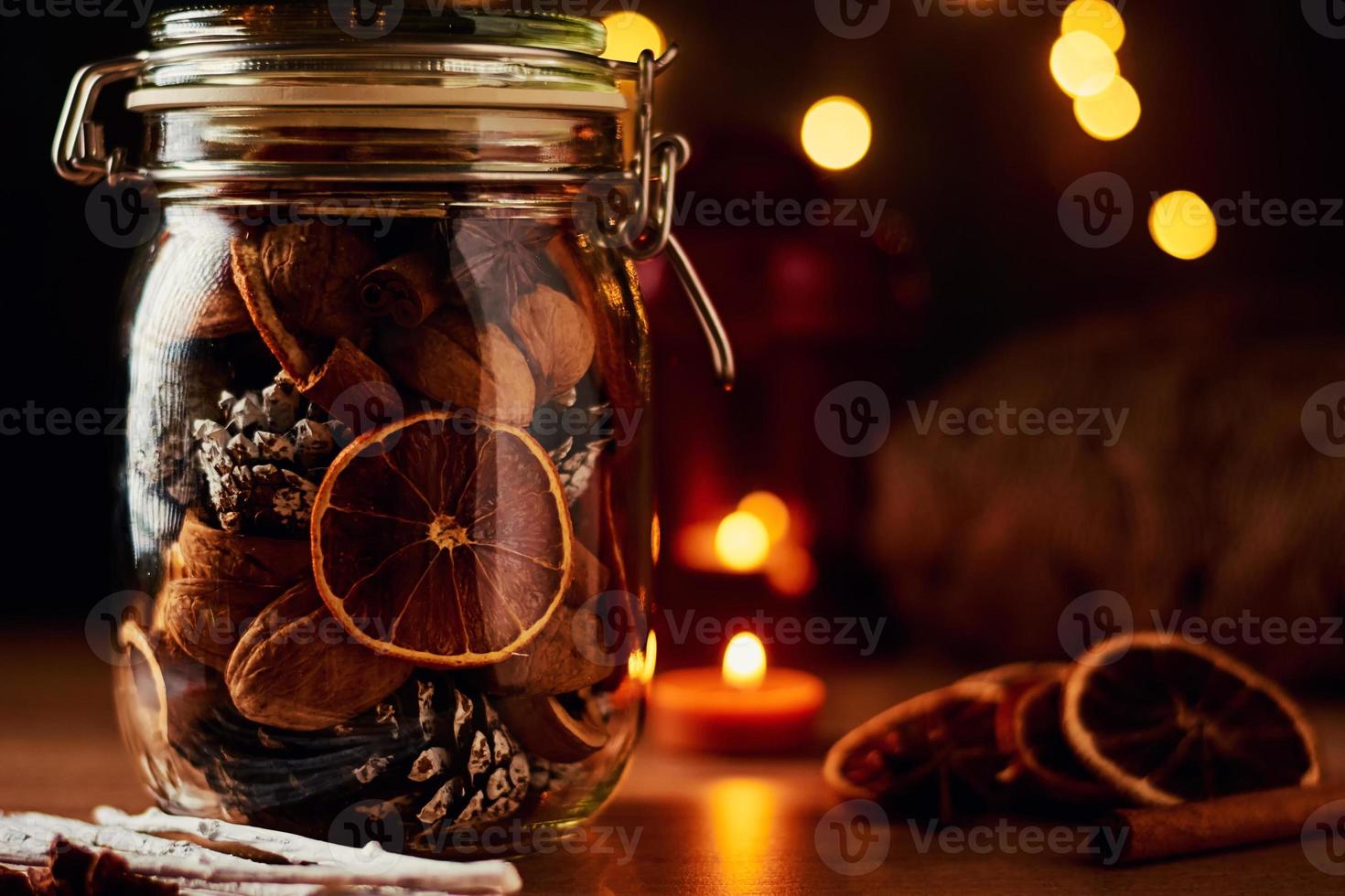 Festive decorations. Glass jar with pine cones and dried oranges on a fairy lights background photo