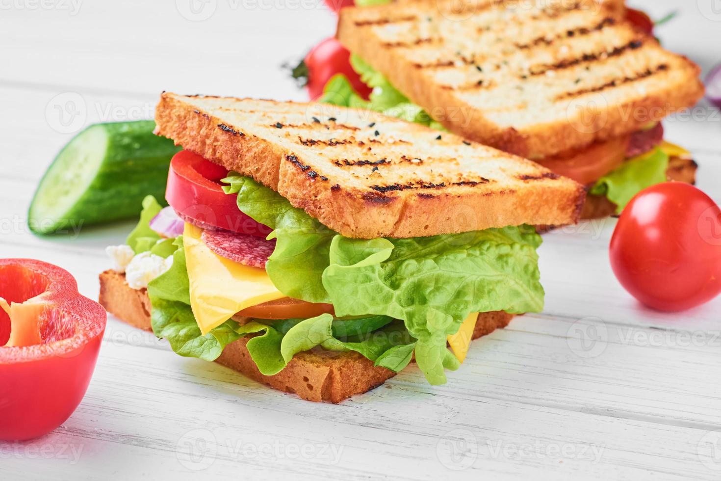 dos sándwiches con jamón, lechuga y verduras frescas sobre un fondo blanco foto