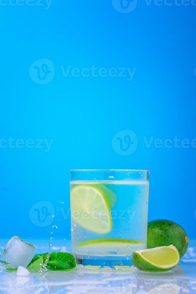 Cóctel con limón y menta fresca en vidrio sobre un fondo azul. foto