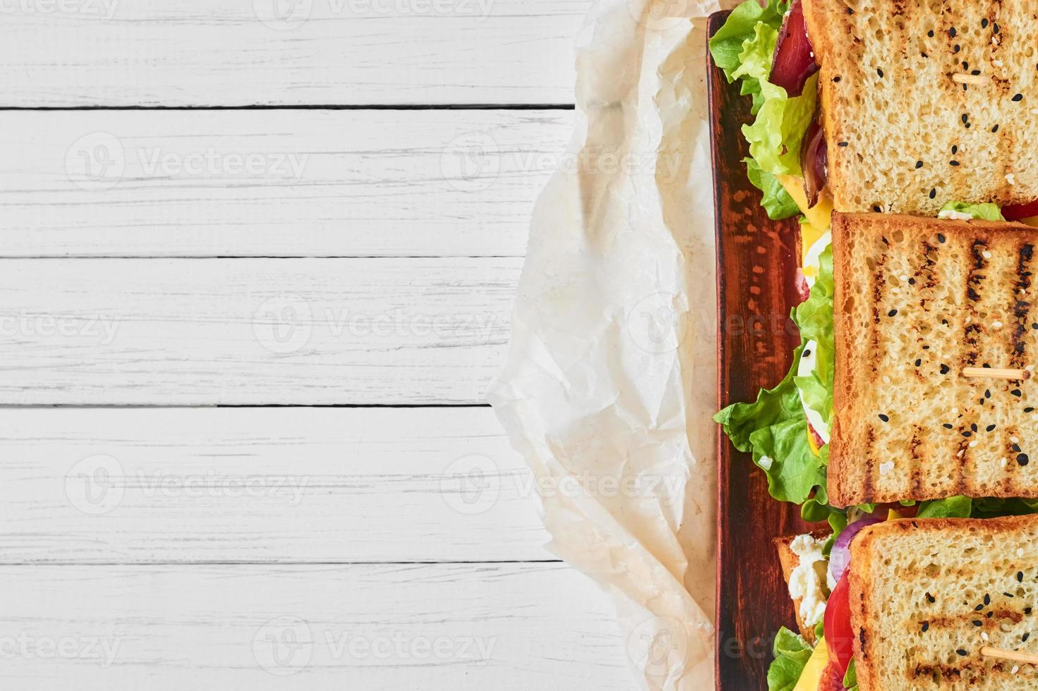 tres sándwiches con jamón, lechuga y verduras frescas sobre un fondo blanco, vista superior con espacio para copiar foto