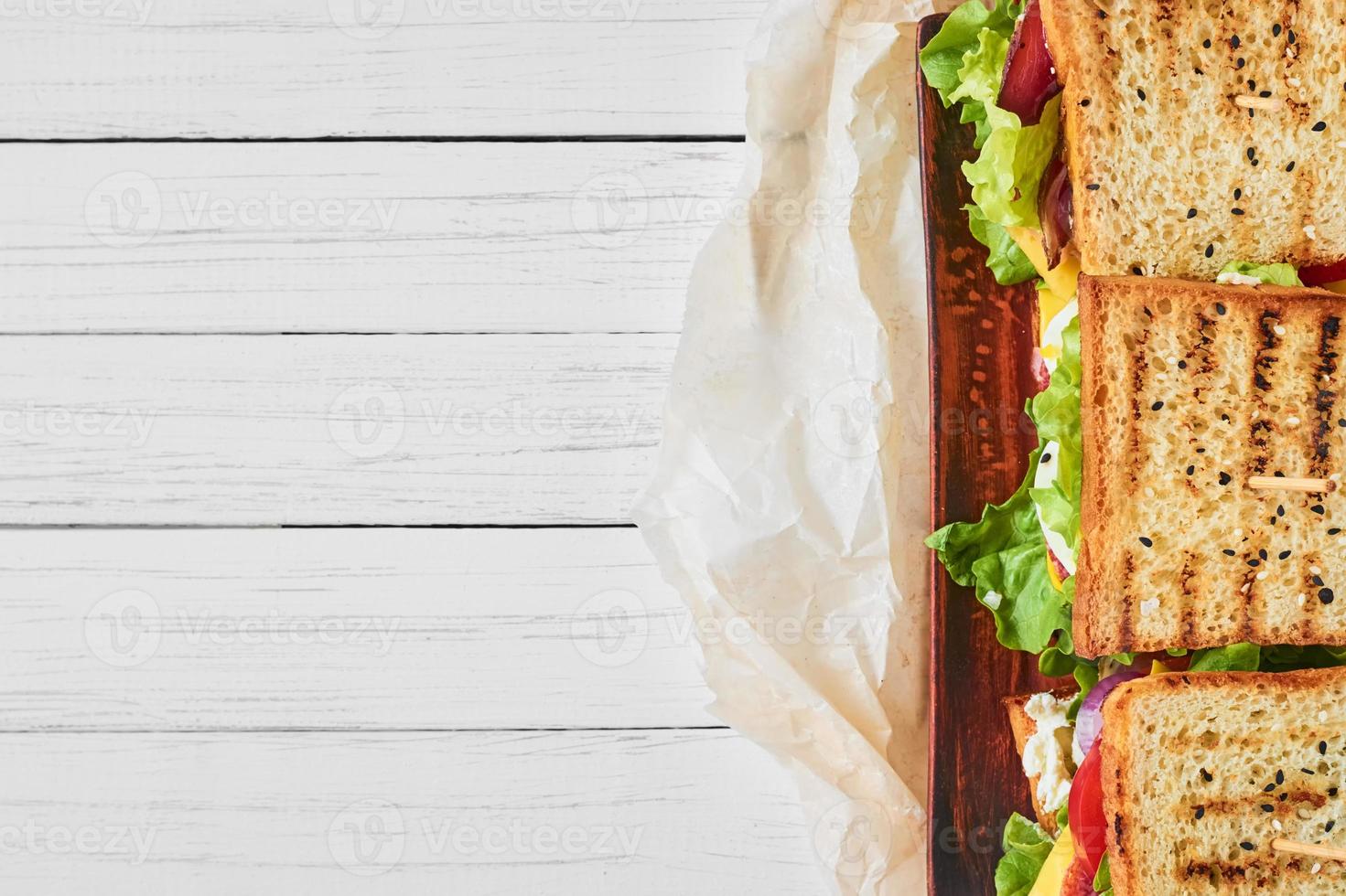 Three sandwiches with ham, lettuce and fresh vegetables on a white background, top view with copy space photo