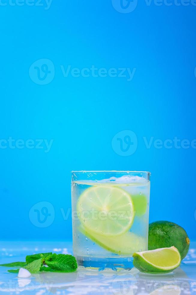 Cóctel con limón y menta fresca en vidrio sobre un fondo azul. foto