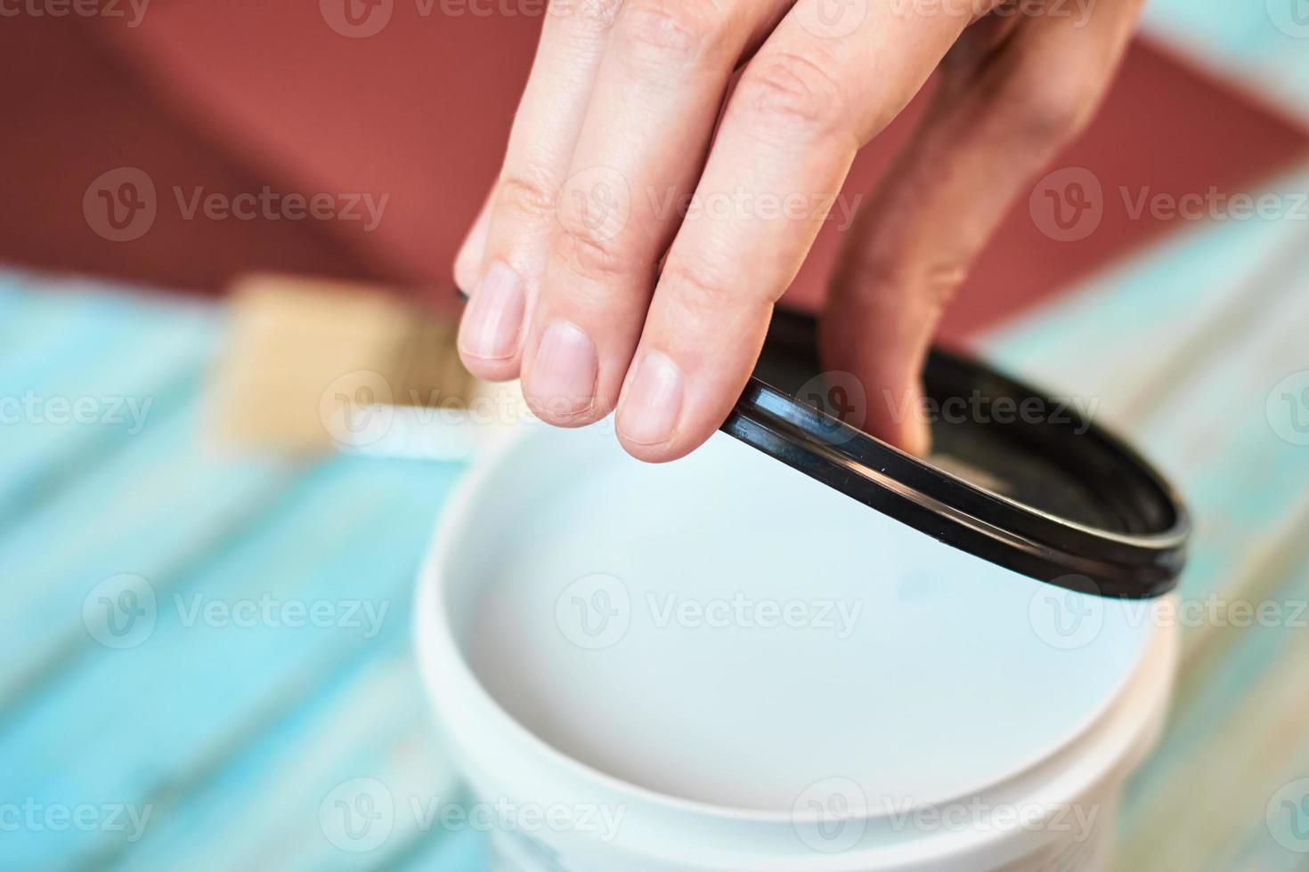 abra a mano una lata de pintura blanca y tablas de madera preparándose para pintar foto