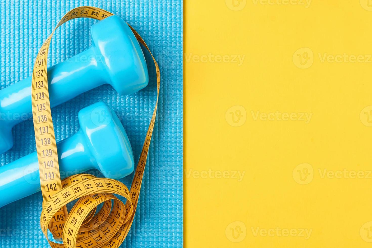 Fitness concept. Dumbbells and measuring tape on a blue and yellow background, top view flat lay photo