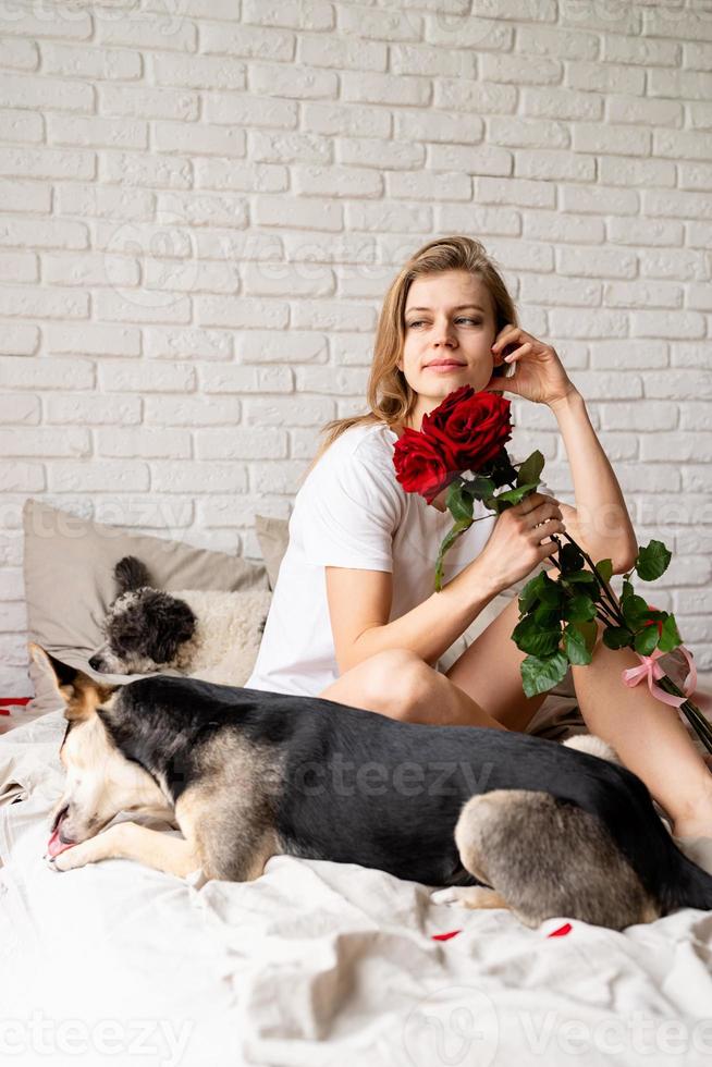 Woman sitting on bed with her funny dog at home and smelling flowers photo