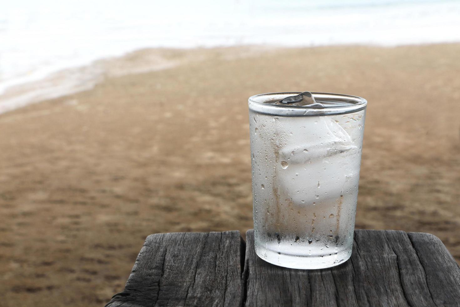 Drink water with cold ice in glass of water on old wooden plank on the beach. photo