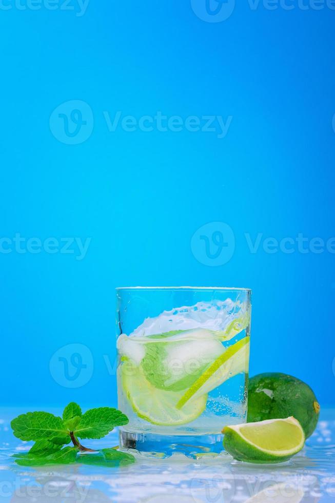 Splashing mojito cocktail with lime and fresh mint in glass on a blue background photo