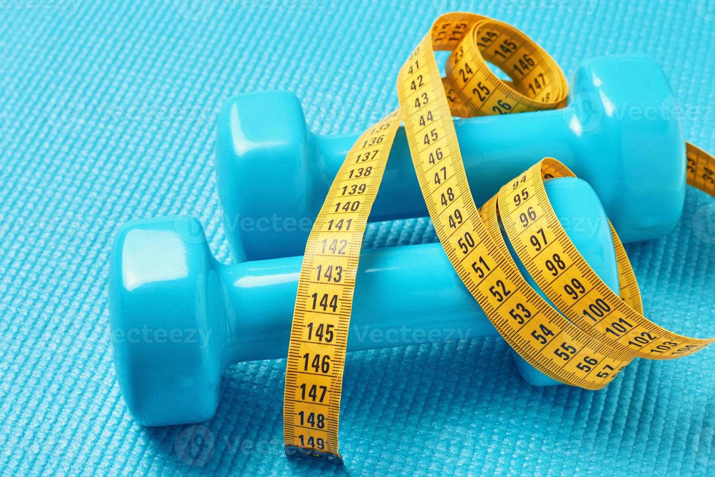 Fitness concept. Dumbbells and measuring tape on a blue background, close up photo