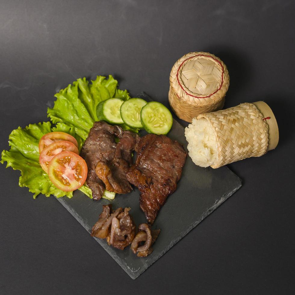 grilled beef with sticky rice on plate over black background studio photo