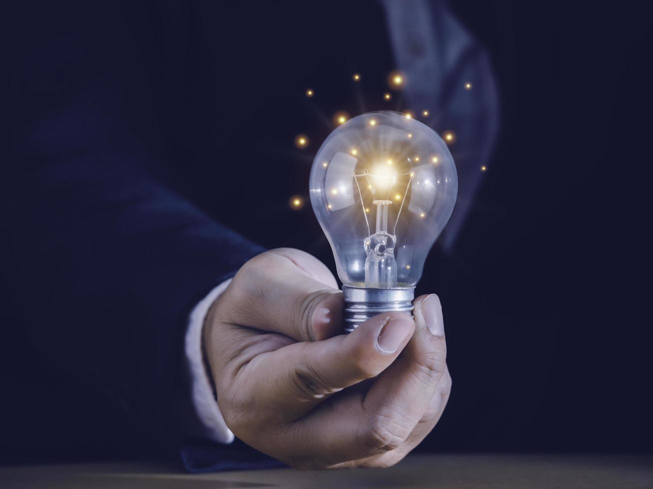 Hand of businessman holding light bulb with fire spark shine glitter for new idea with innovation and inspiration, communication and technology in science concept. photo