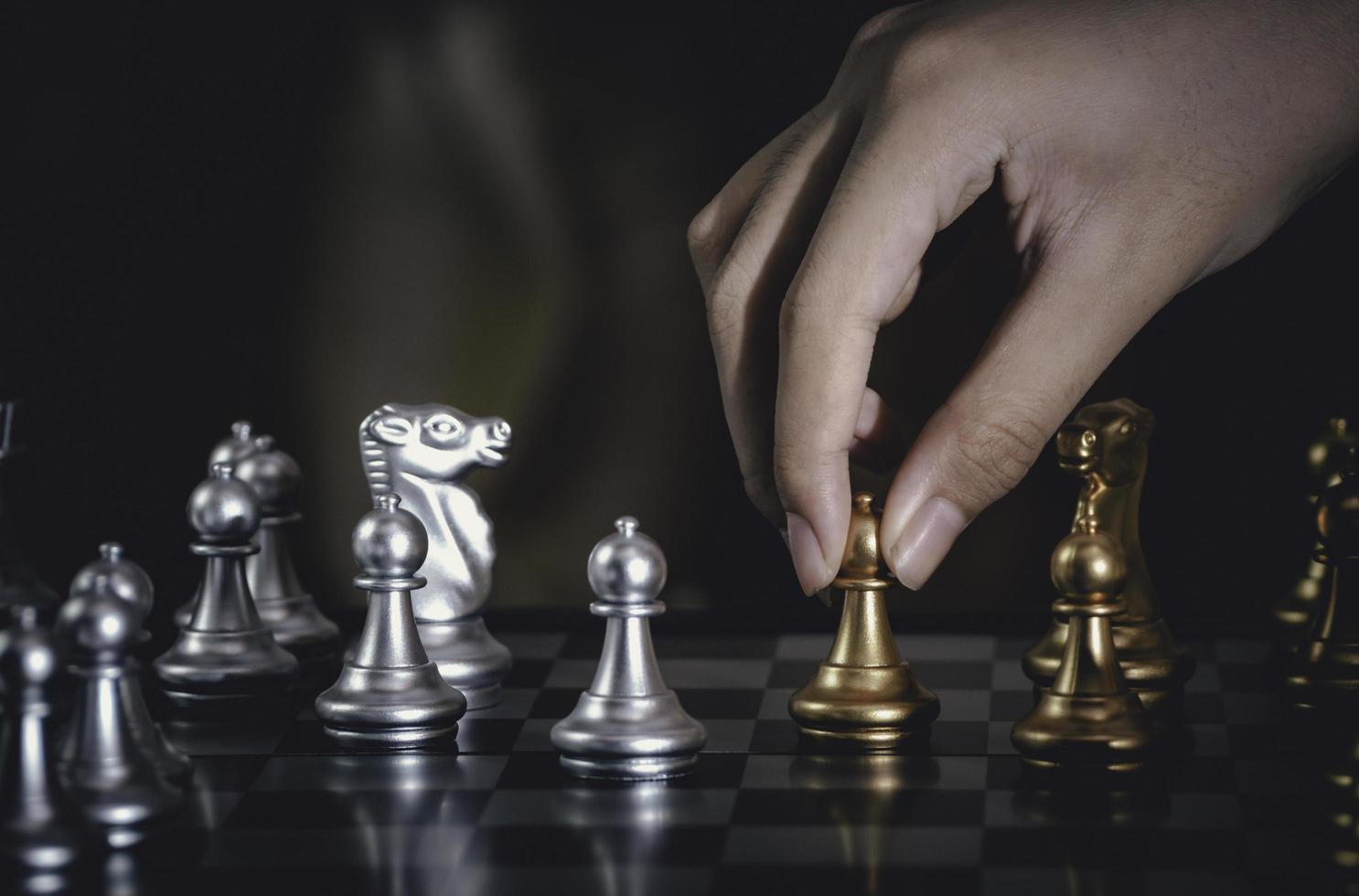 Hand businessman moving silver pawn chess fighting on board with gold chess background. successfully in the competition with technology network background. Management or leadership strategy concept. photo