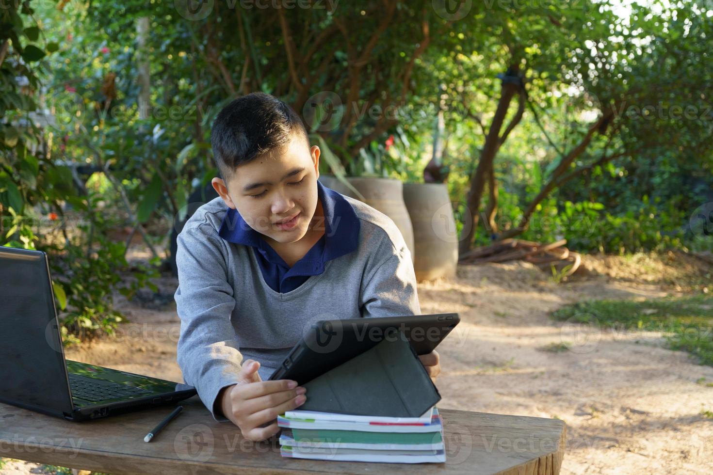 boy studying online looks at the tablet with interest on a wooden table at the country house. concept online education countryside area and work from home photo