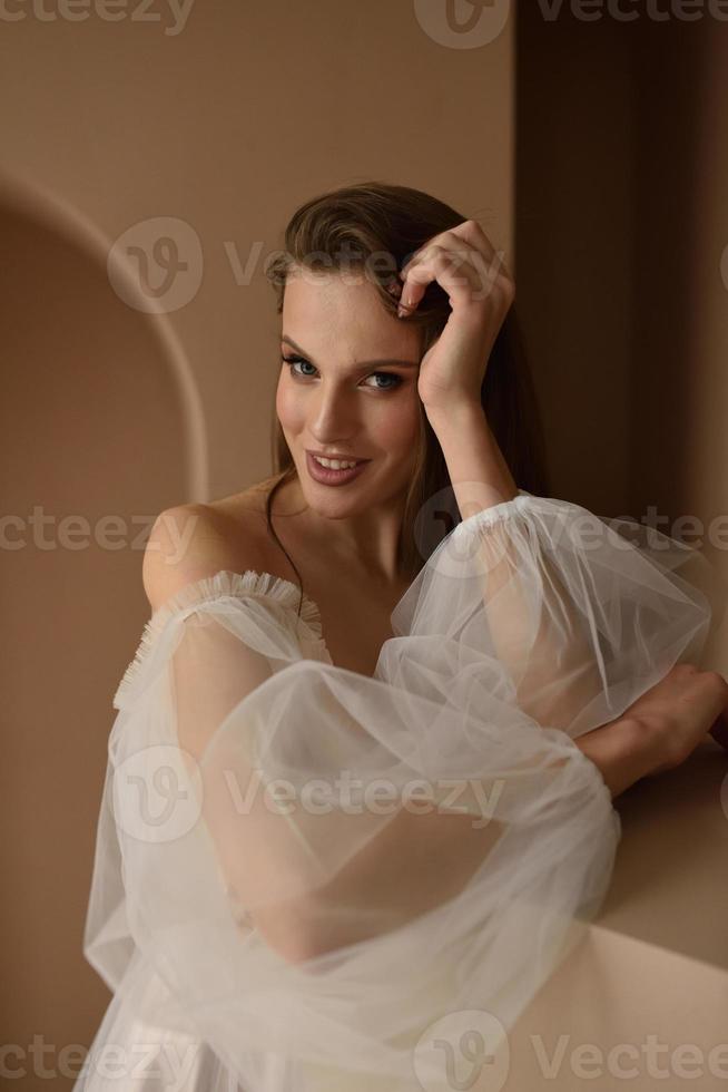 Portrait of a beautiful bride in full growth in the studio on a white background. The woman stands with her back and looks into the frame. photo