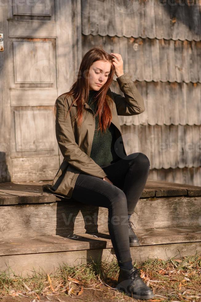 A young girl sits on the steps of a wooden house entrance. photo