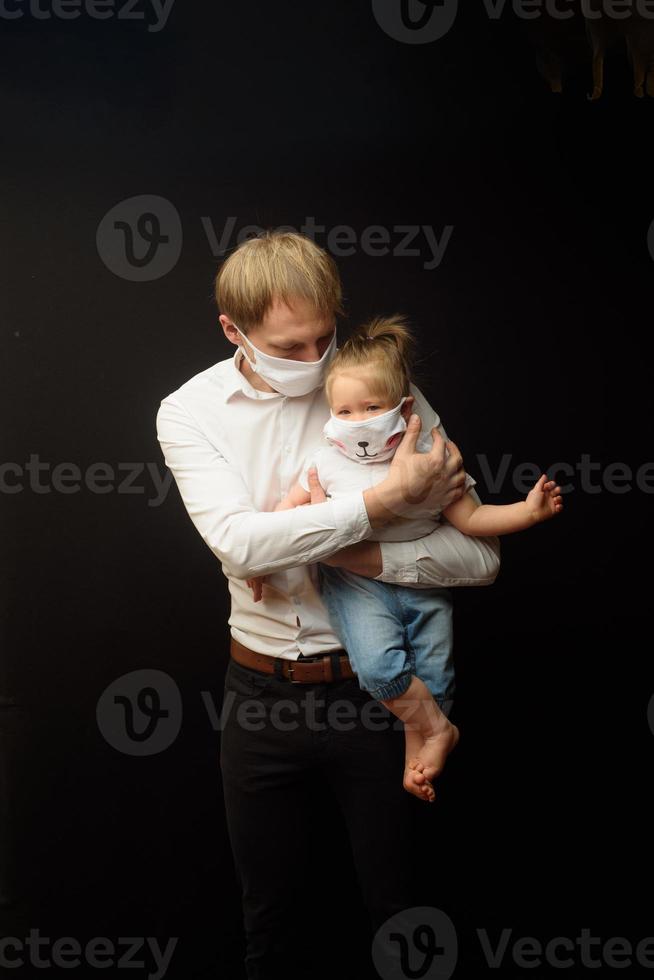 padre con una máscara médica sostiene a su pequeña hija. el concepto de proteger a los niños durante la epidemia de coronavirus foto