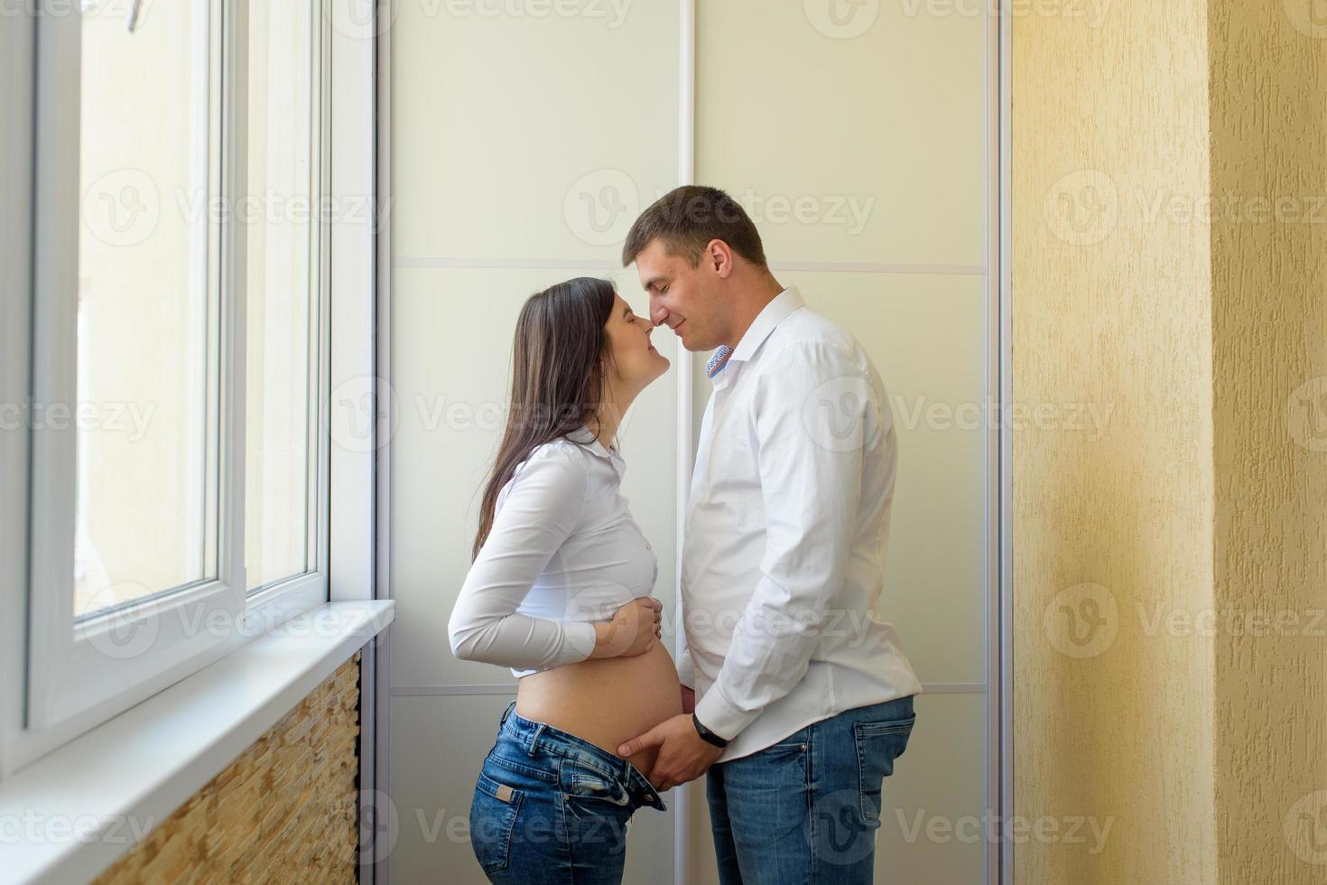 A man and a pregnant woman are sitting hugging on the couch. photo