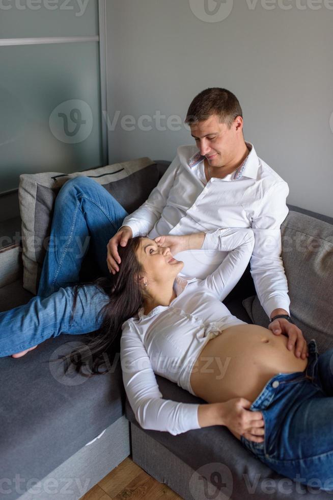 A man and a pregnant woman are sitting hugging on the couch. photo
