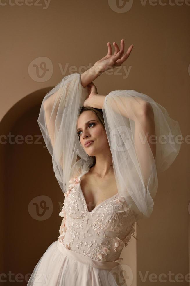Portrait of a beautiful bride in full growth in the studio on a white background. The woman stands with her back and looks into the frame. photo