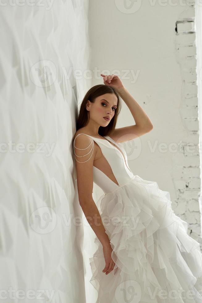Portrait of a beautiful bride in full growth in the studio on a white background. The woman stands with her back and looks into the frame. photo